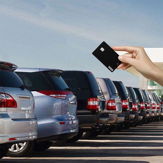 Hand holding credit card in front of car lot